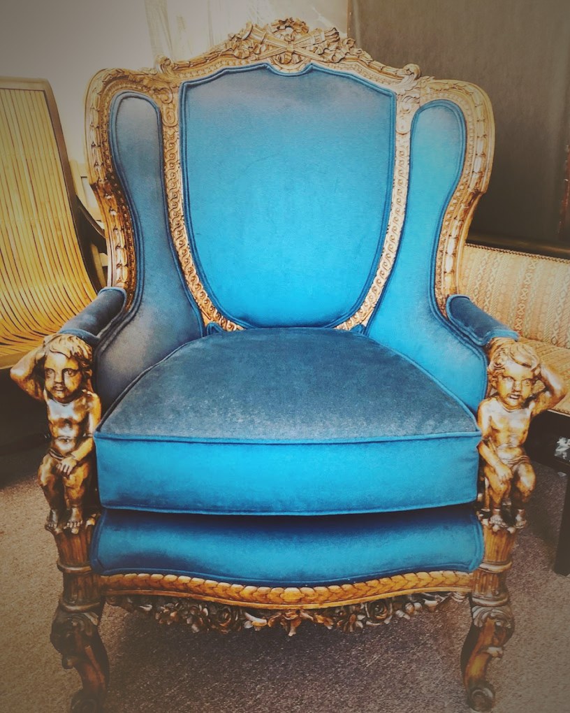 An ornate carved wingback chair restored in blue velvet